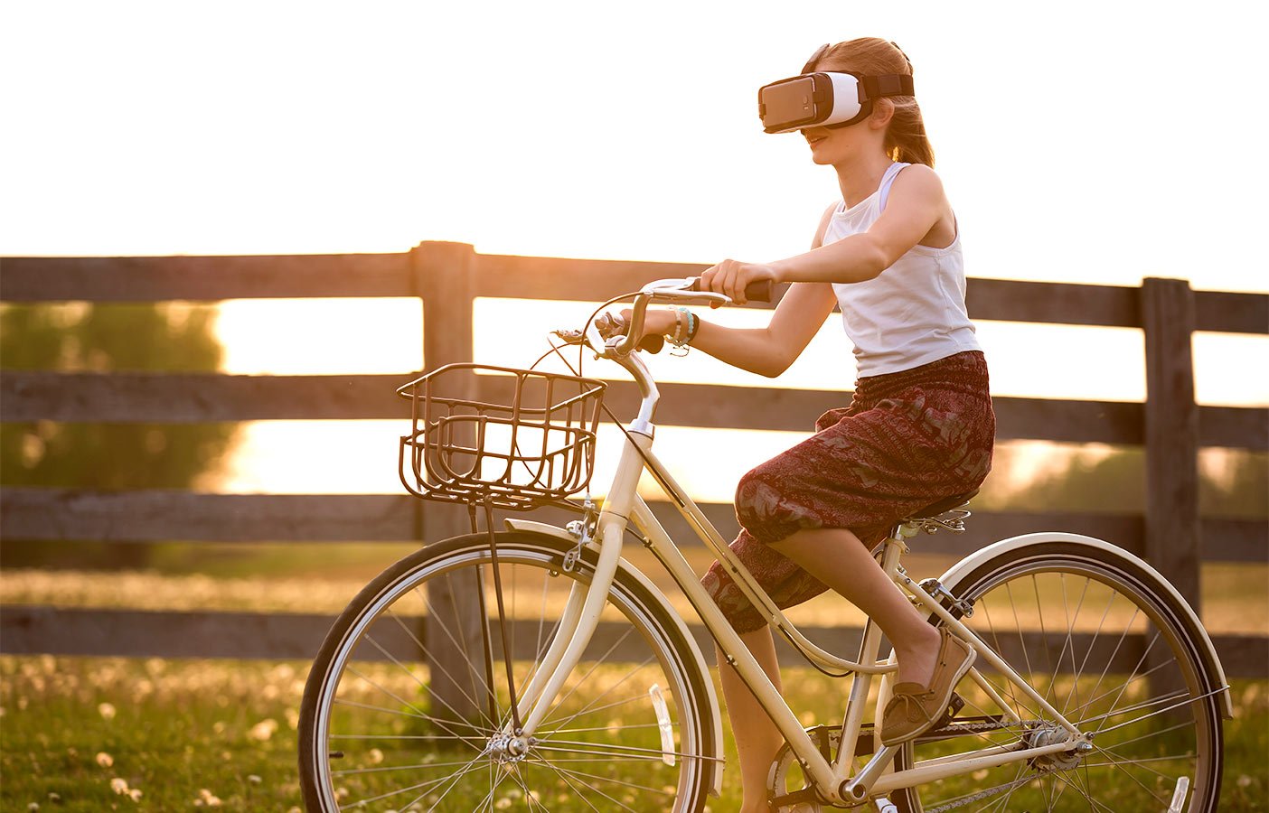 Kind mit Virtual-Reality-Brille fährt auf Fahrrad an Zaun entlang