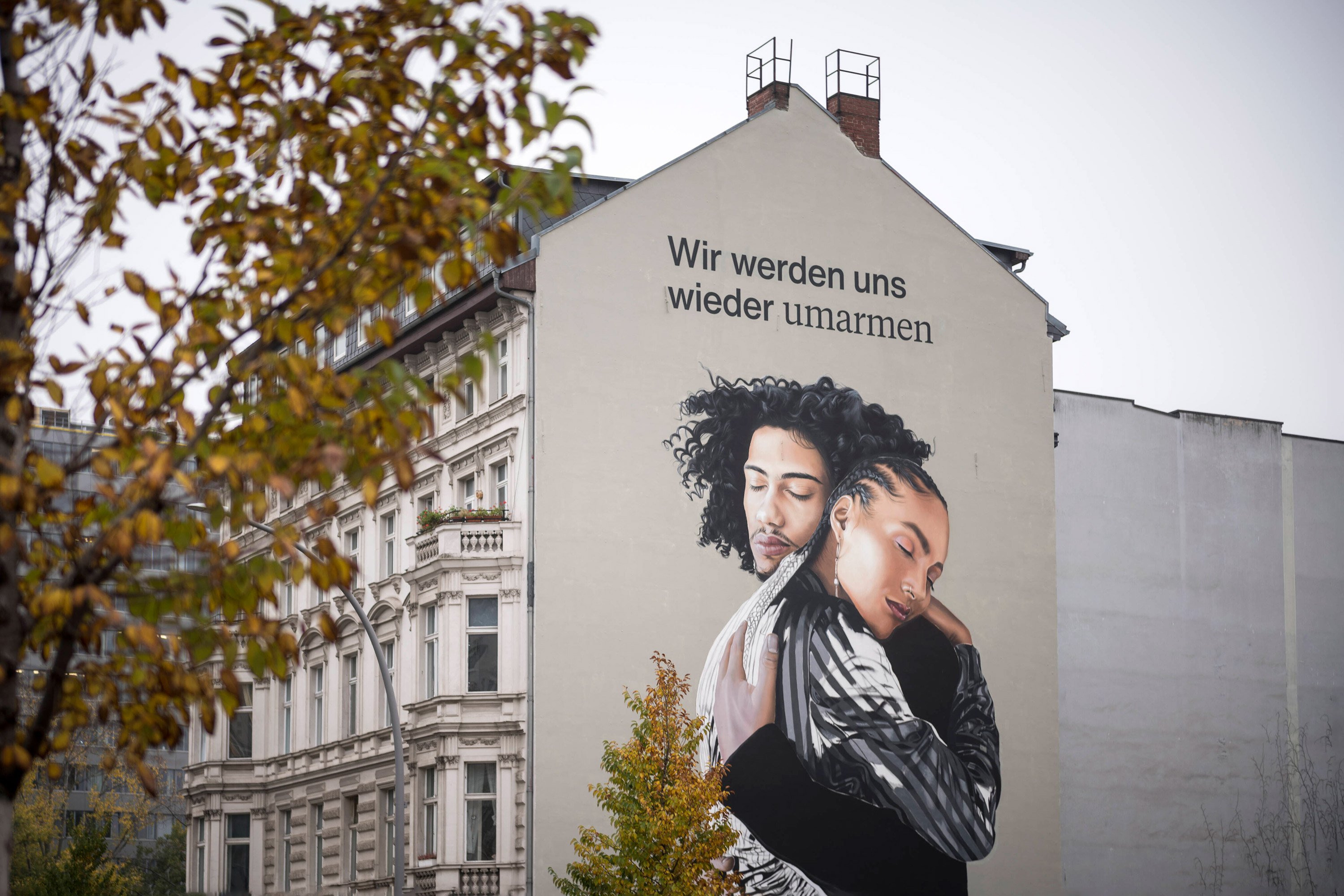 Hausfassade mit Zeichnung von Umarmung und Spruch "Wir werden uns wieder umarmen"