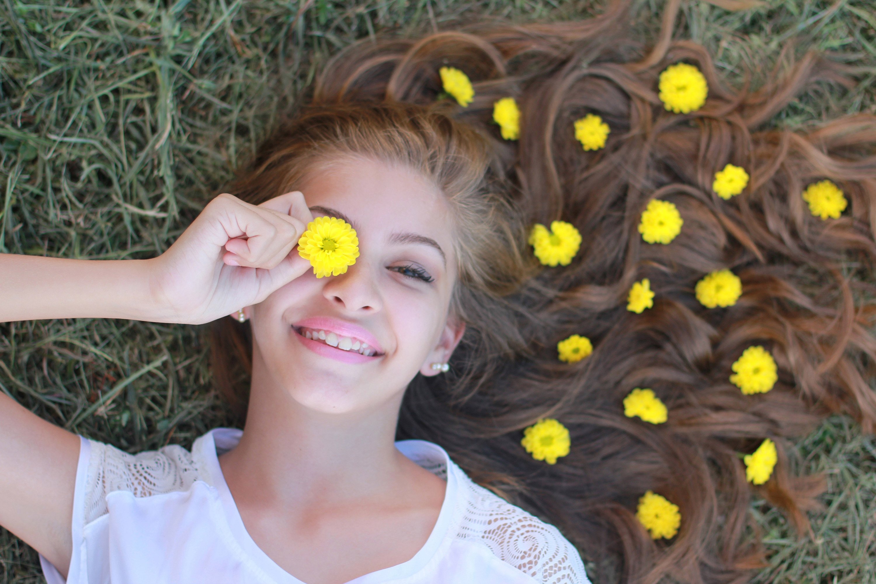 Frau mit gelben Blumen im Haar liegt auf Wiese 